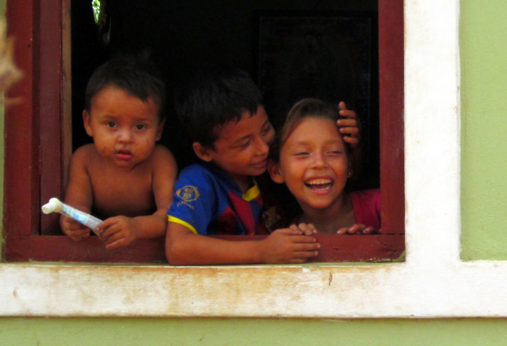 Adriana, at the window of her home with her two little brothers, Brian and Andi